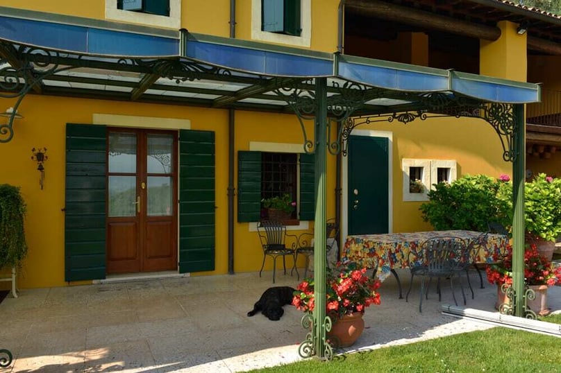 A photo of the front entrance to a colorful luxury home featuring double doors and green shutters. 