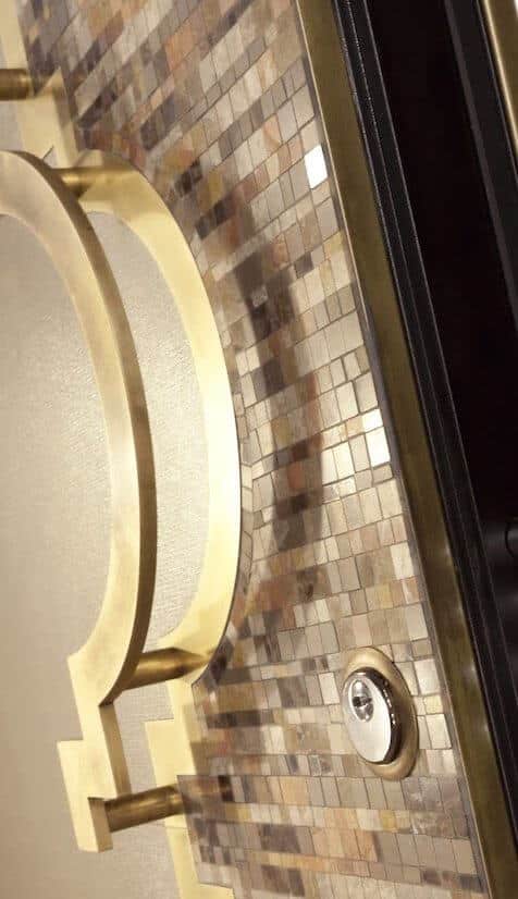 A close-up photo of a custom security door in a luxury home featuring mosaic tile and gold hardware.