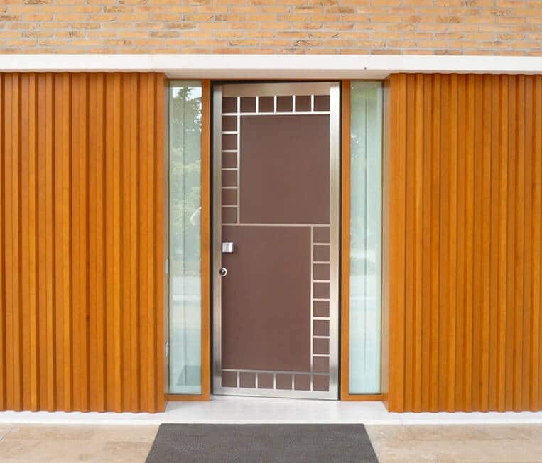 A photo of a custom security door featuring a large letter “S” in stainless steel.