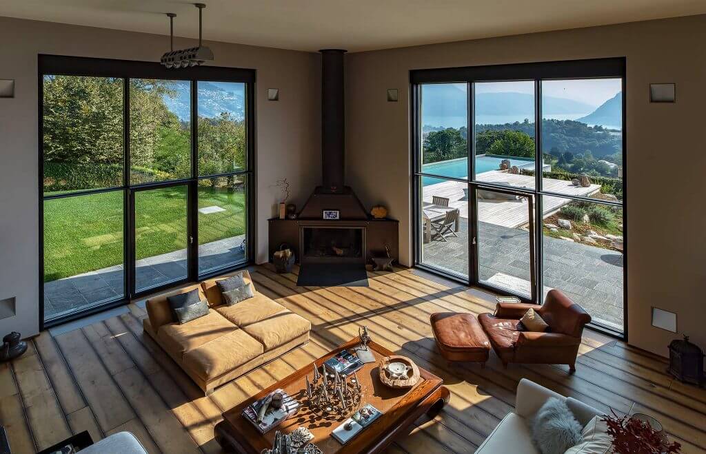 A photo of a spacious living room featuring floor-to-ceiling windows that overlook a backyard with a pool.