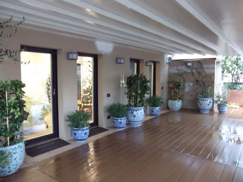 A photo of a covered patio on a luxury home with multiple glass doors leading outside.