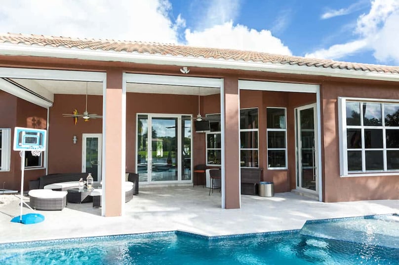 A photo of the back of a luxury home, complete with a beautiful patio, a pool, and large security windows.