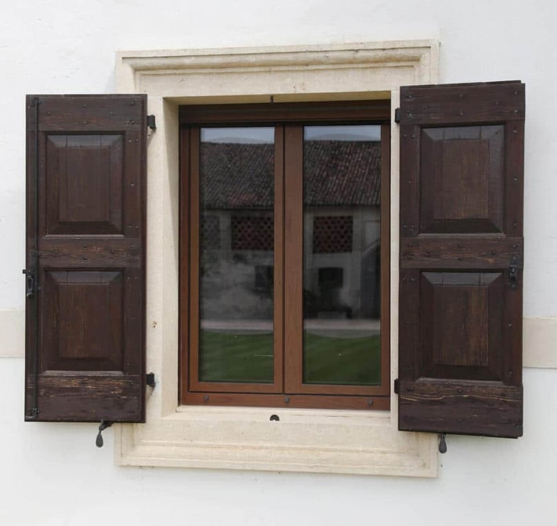 A photo of a hurricane certified window installed in a luxury home with walnut stained shutters. 